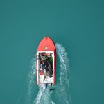 Top view of a red motorboat with fishermen navigating open turquoise waters.